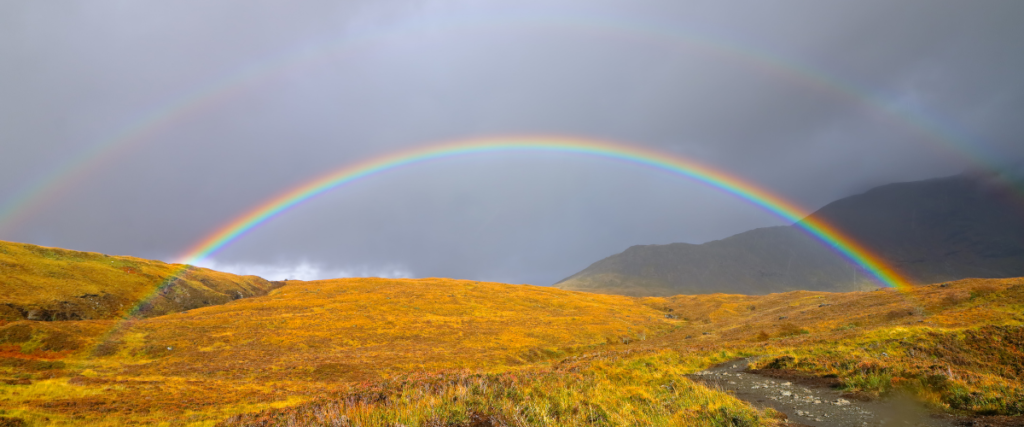 a landscape photograph from the scottish highlands with a double rainbow in the sky 